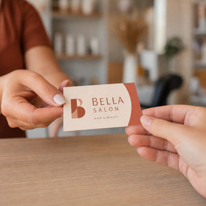 Premium Matte Business Cards in use - being handed across a light wooden salon reception counter from one hand to another