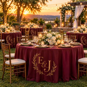 Custom printed burgundy round tablecloths with a gold monogram at an outdoor wedding