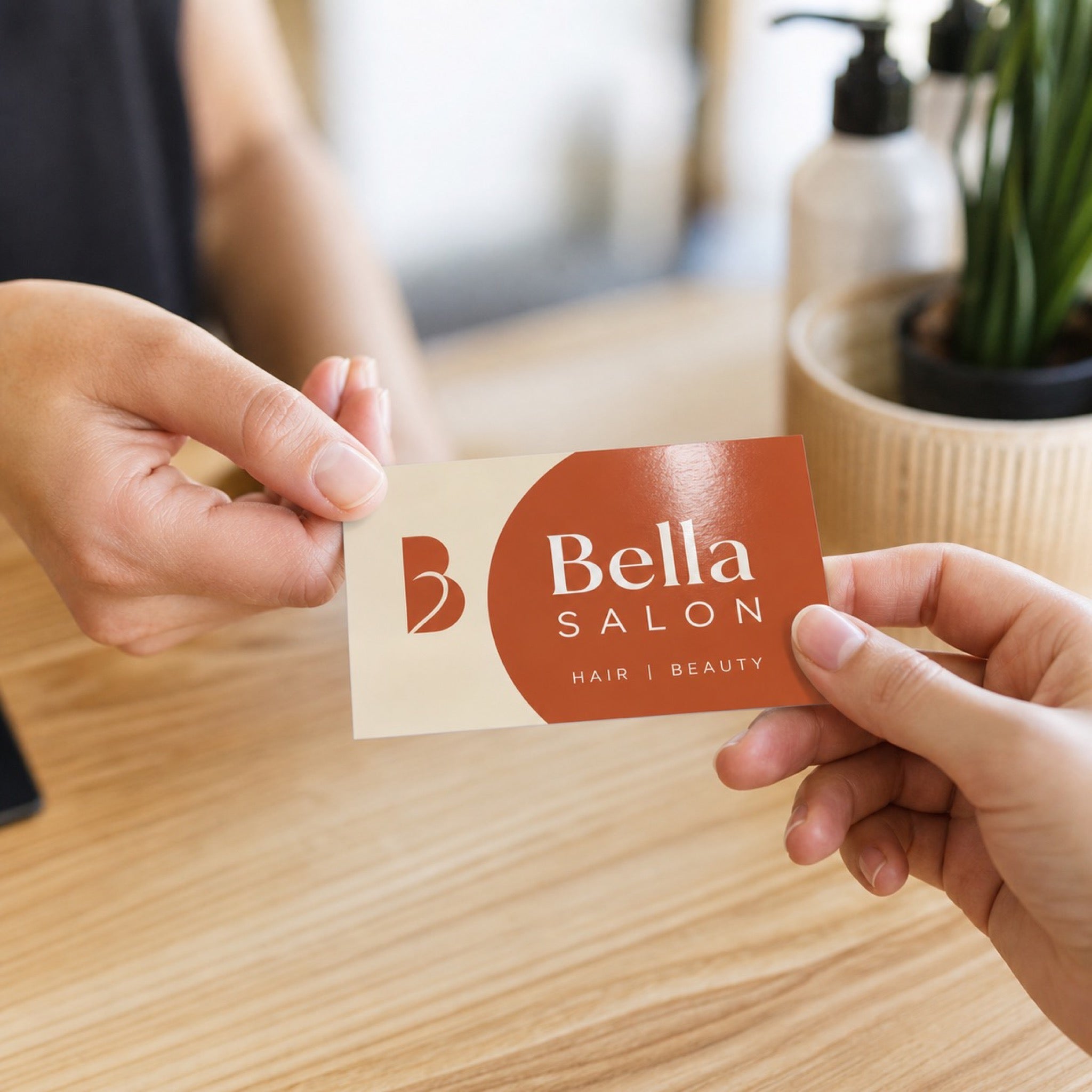 Glossy Business Cards in use - being handed across a light wooden salon reception counter from one hand to another