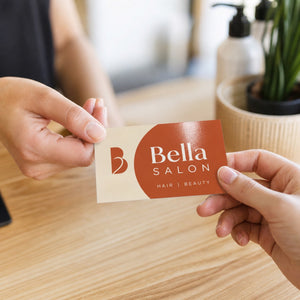 Glossy Business Cards in use - being handed across a light wooden salon reception counter from one hand to another