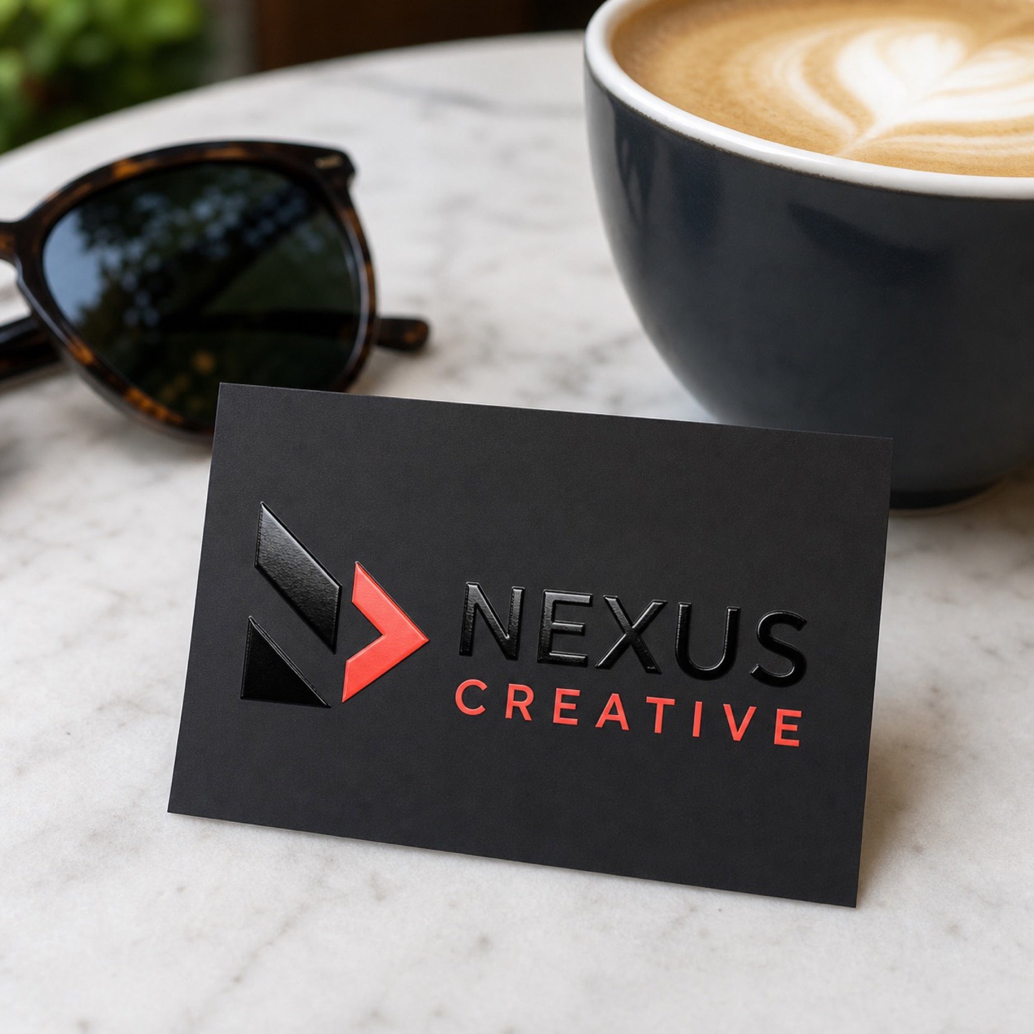 Spot UV Business Cards in use - resting on a marble cafe table next to a flat white coffee and a pair of sunglasses
