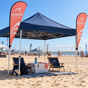 Two custom teardrop tent flags clamped to the front legs of a beach canopy